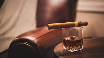 A cigar rests atop a glass of whiskey