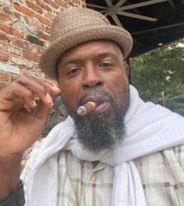 Boxing world champion, Yahya McClain wearing a hat and smoking a cigar
