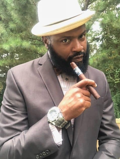 Boxing world champion, Yahya McClain in a hat and suit while holding a cigar