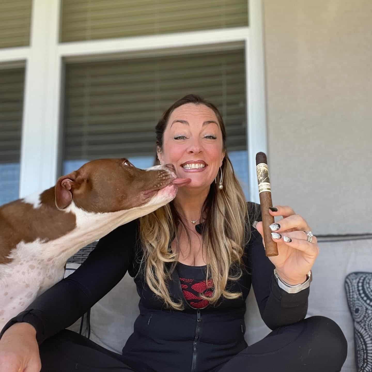 Holly Primc holding a cigar and smiling with her dog.