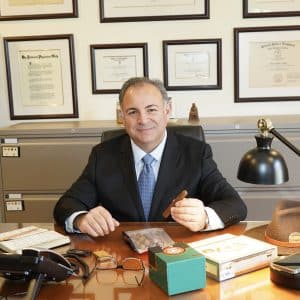 Dr. Gaby Kafie seated behind a desk and holding a cigar