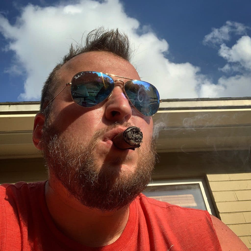 Jonathan Carney wearing sunglasses outside with a cigar in his mouth