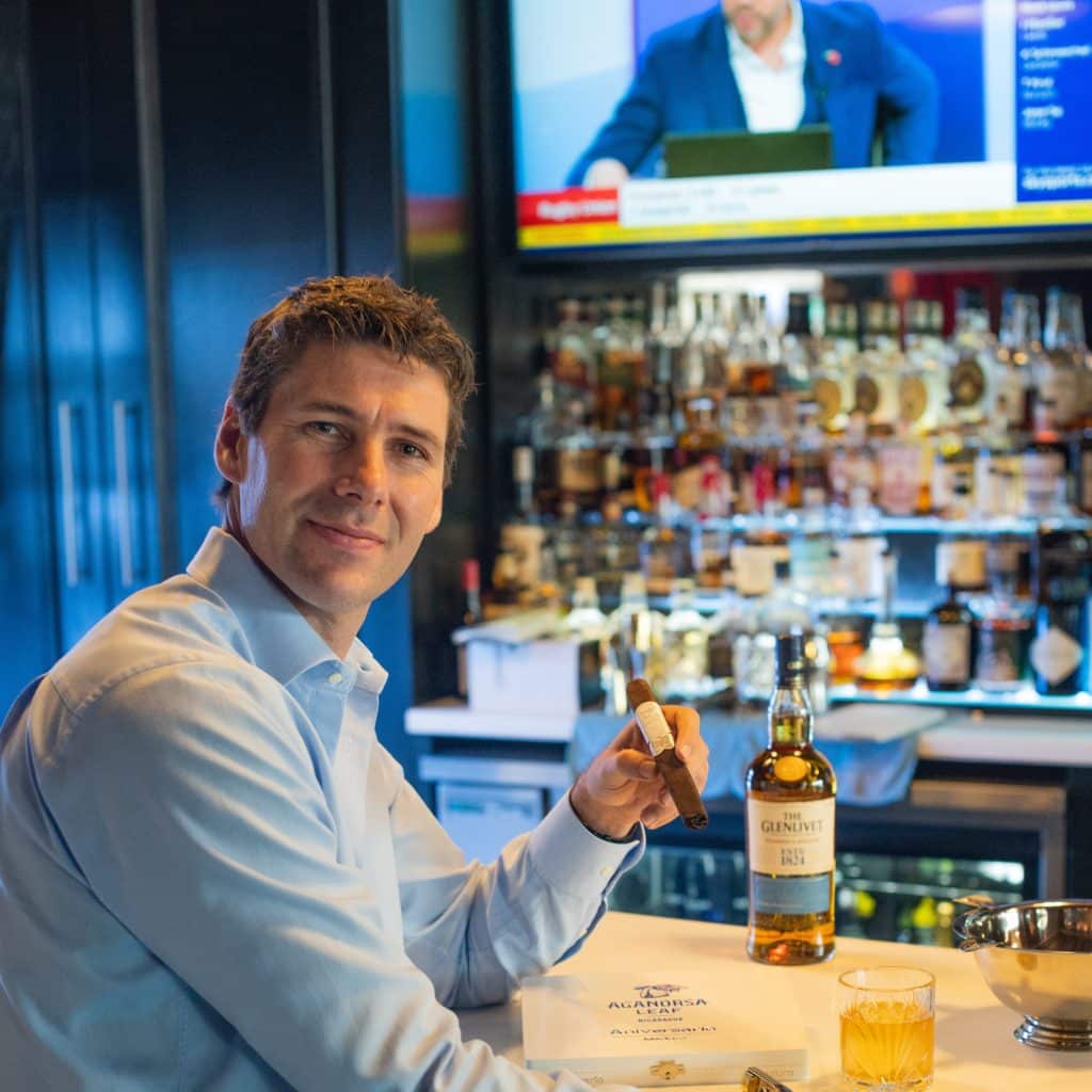 Terence Reilly sitting at a bar, facing forward, and holding a cigar.